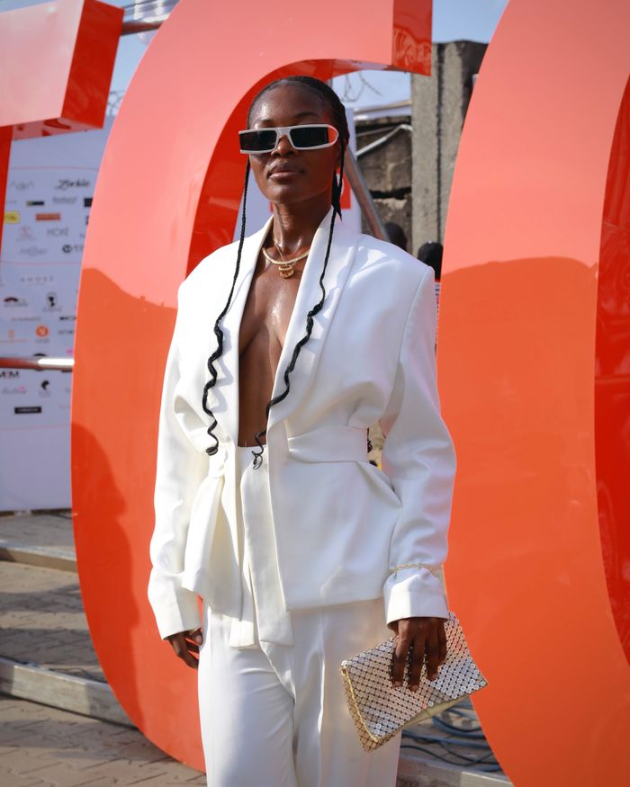 A fashionable woman in a white suit and sunglasses at an outdoor fashion event.