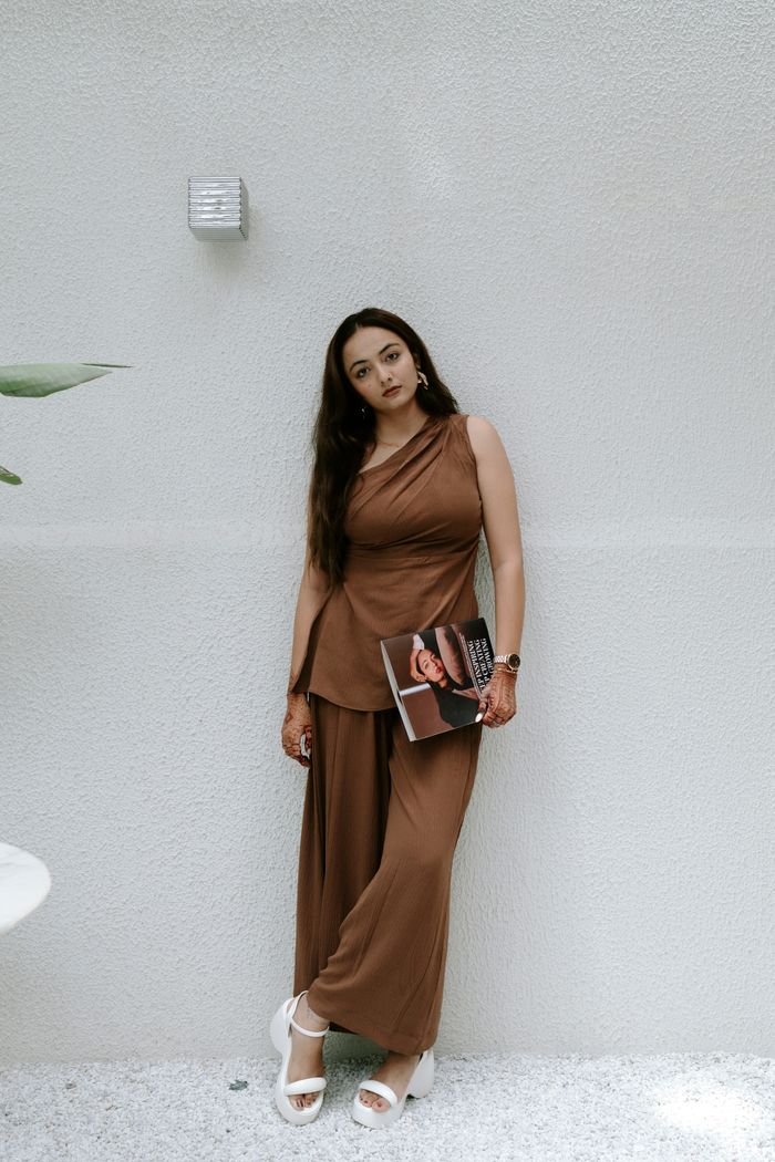 Fashionable woman in brown outfit posing indoors against a minimalist wall in Surat.