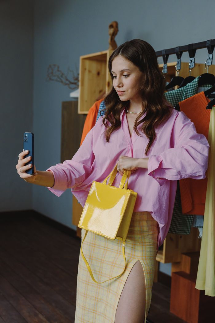 Stylish woman in a pink shirt takes a selfie, showcasing her outfit with a yellow handbag.